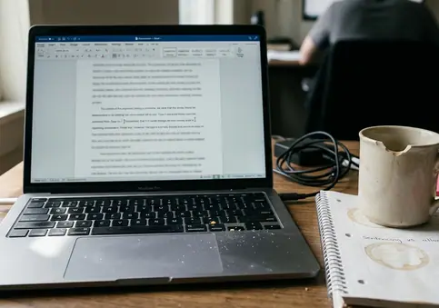 Home office writing setup with laptop open to a half-drafted paragraph, screen slightly tilted, cursor